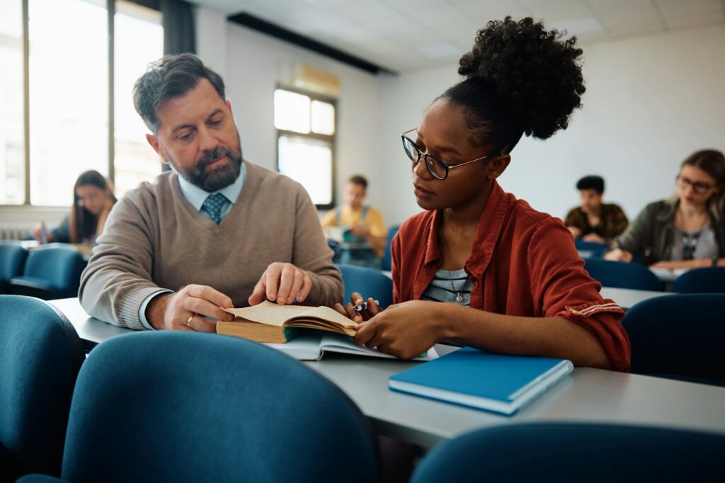 Black college student learning with teacher's assistance in the classroom.